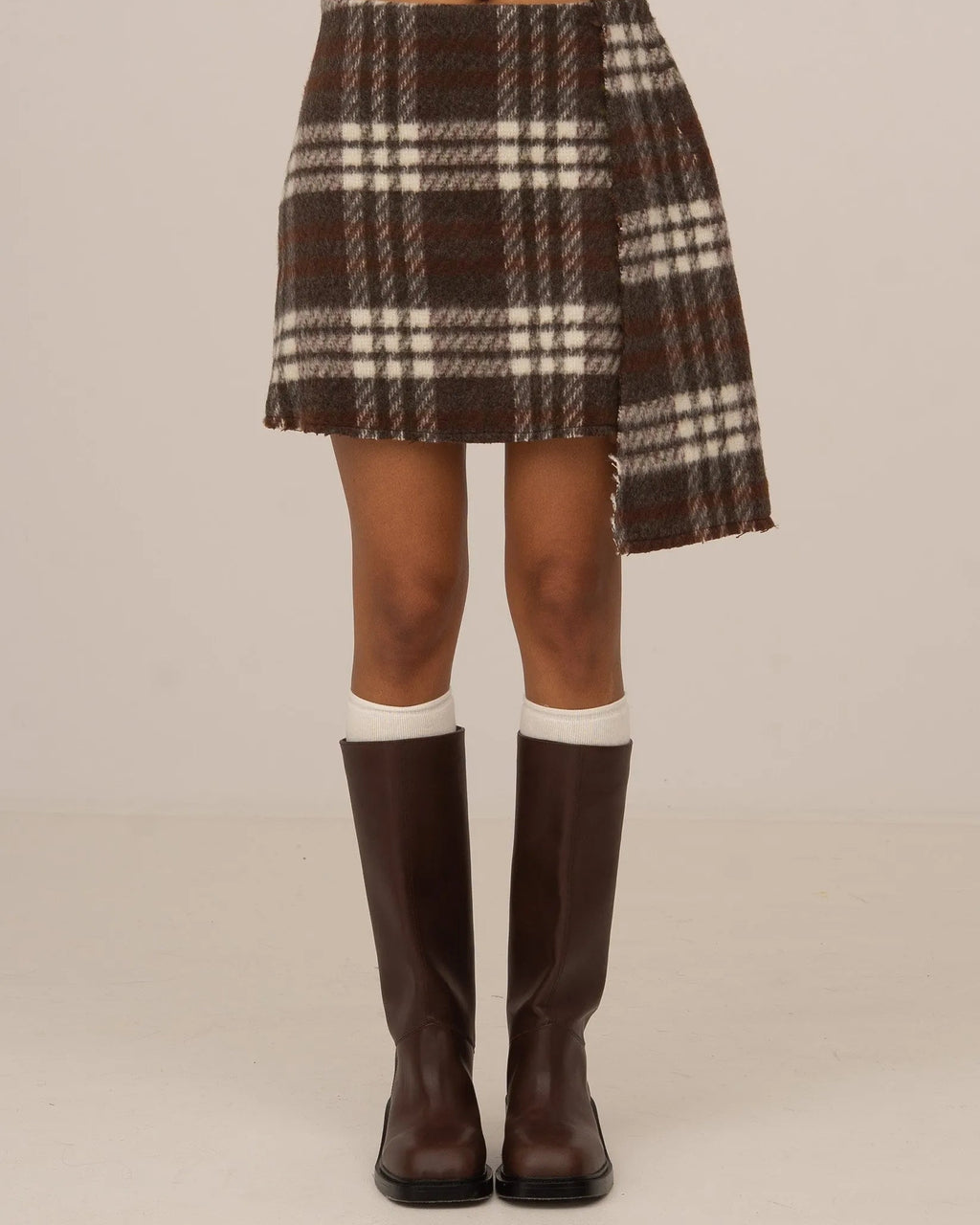 Barefoot model wearing a brown plaid mini skirt by māre Carmen Says, showcasing the stylish, high-waisted design and fabric details.